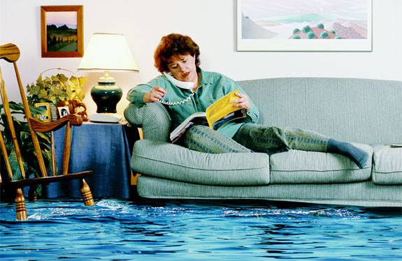 A women sitting on her couch with water all over the floor looking for help by going through her phonebook